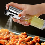 A person pressing the pump of a sleek glass kitchen oil sprayer to mist a fine layer of olive oil over a fresh salad.